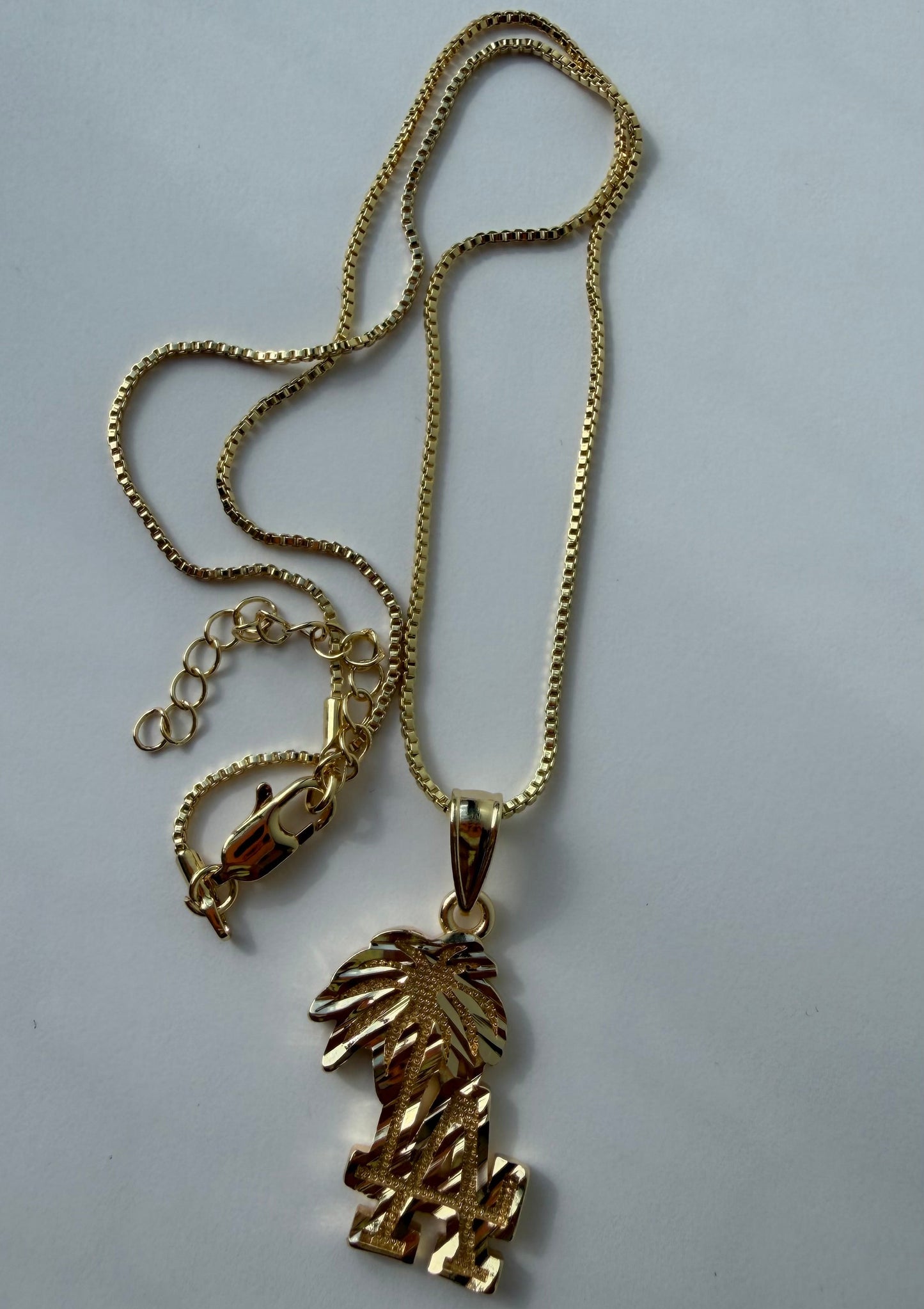 A gold-tone chain necklace with a textured, leaf-like pendant, displayed on a plain light gray background.