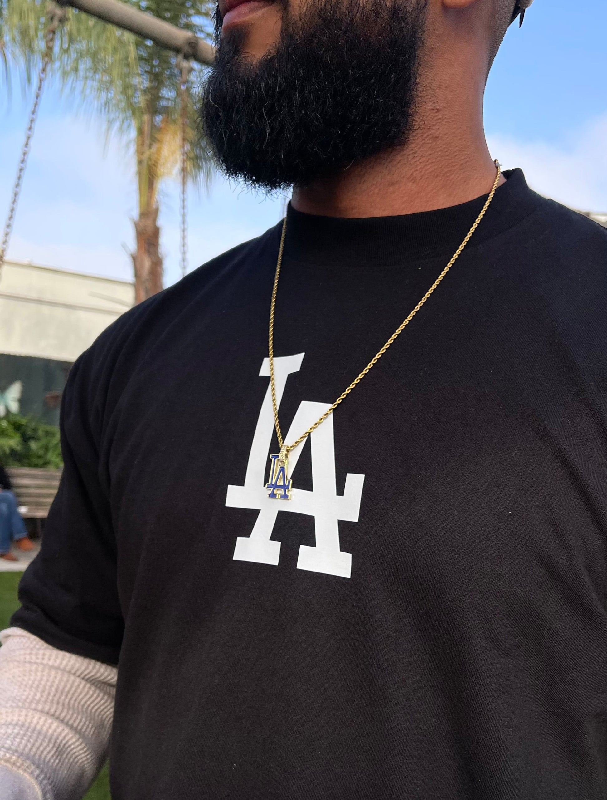 Person wearing a black t-shirt with a white logo, holding a cup outdoors.